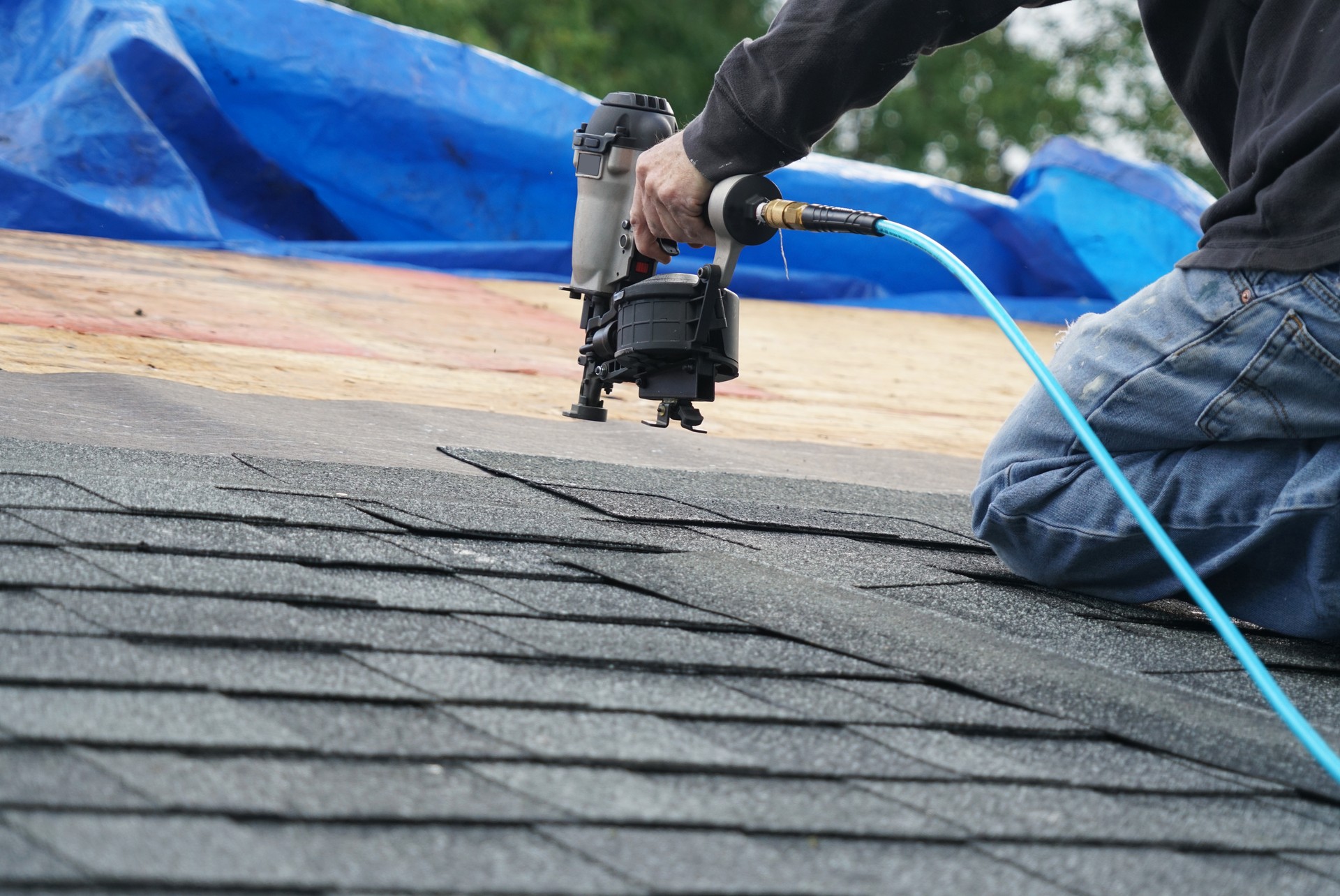 handyman using nail gun to install shingle to repair roof